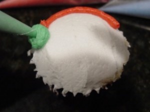 Snowm cupcake with green earmuffs being piped on
