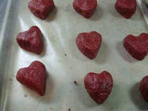 Heart shaped red velvet cake balls on lined baking sheet